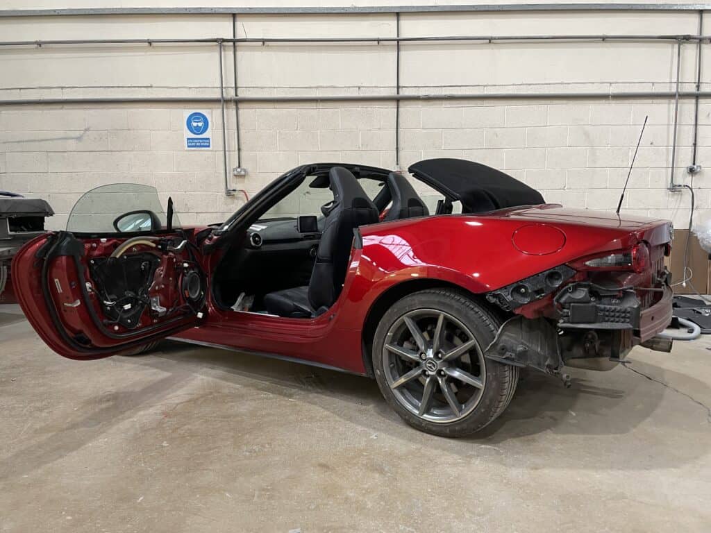 Damaged red convertible car with front-end and side impact, undergoing repair in a garage.