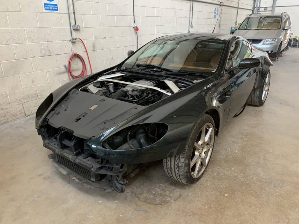 Damaged sports car with front-end impact, undergoing repair in an auto body shop.