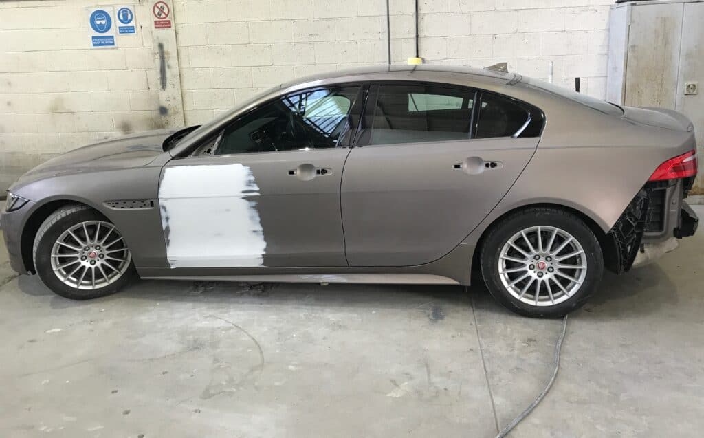 Damaged silver sedan undergoing repair with primer on the door panel.