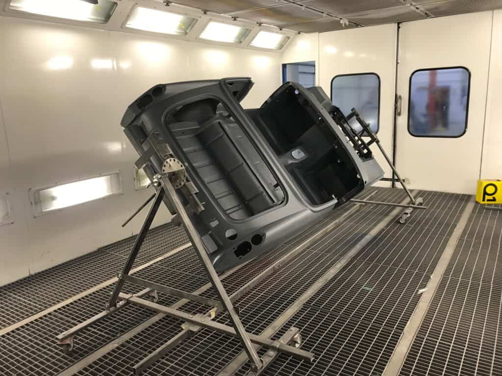 Car body shell undergoing repair in spray booth at auto repair shop.