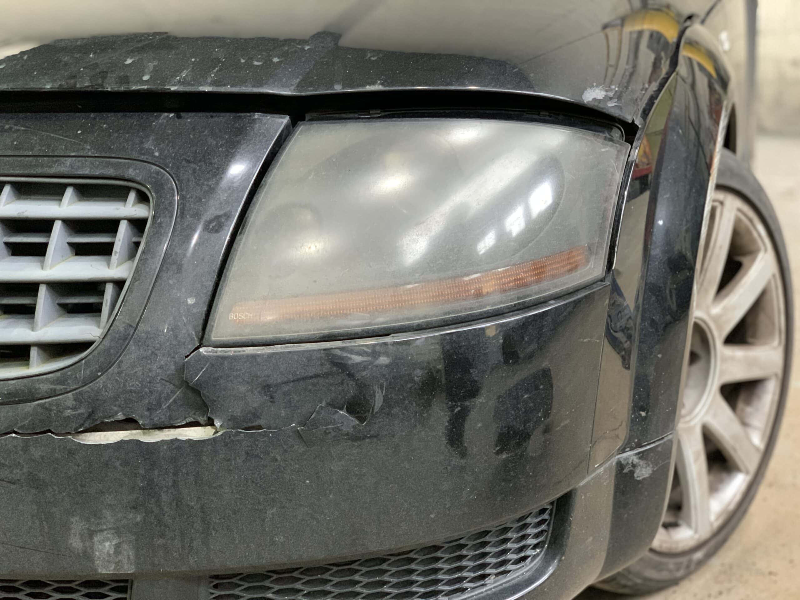 Damaged front bumper and headlight of a black car after a collision.