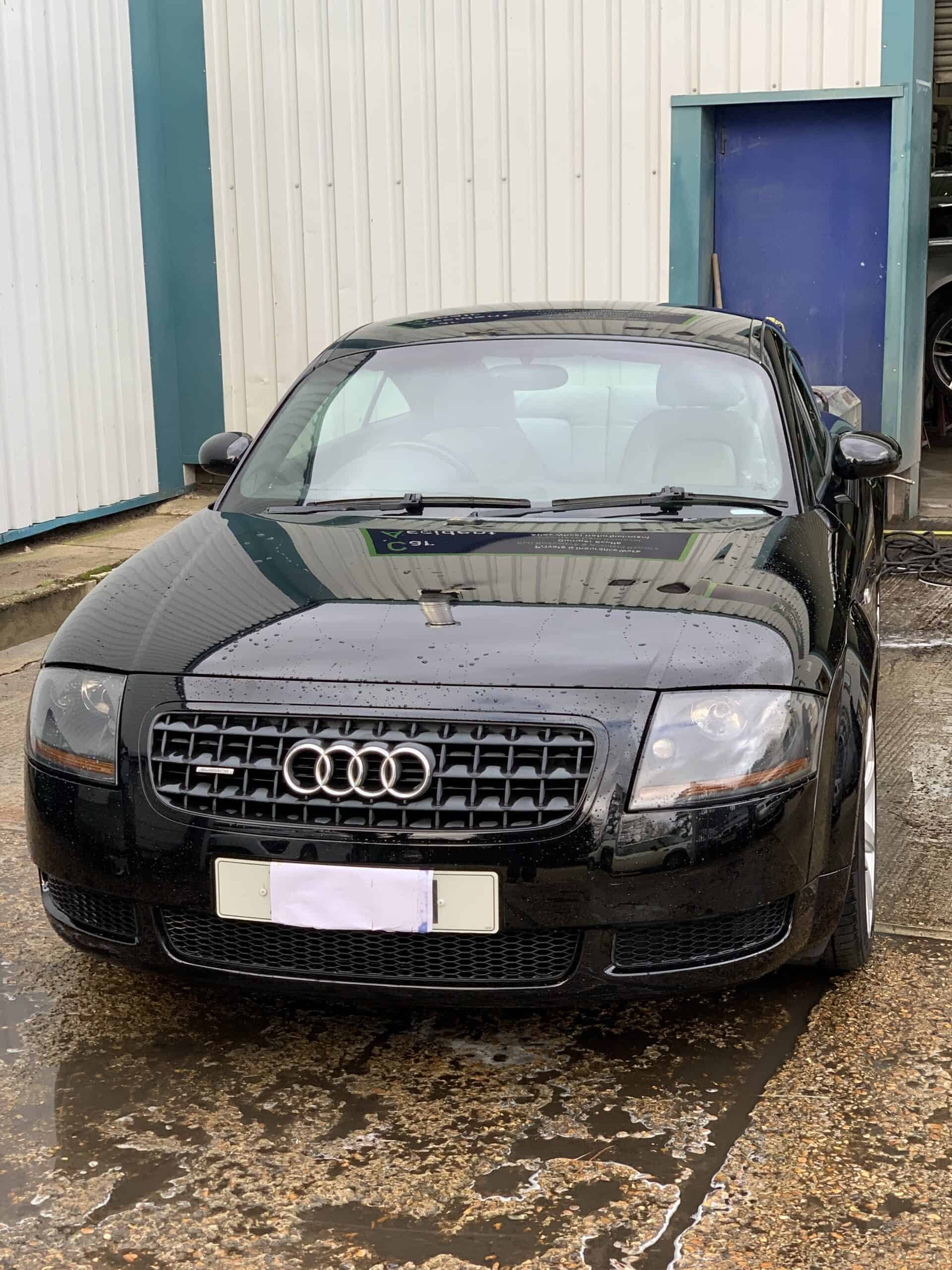 Black Audi car with front-end damage after accident at repair shop.